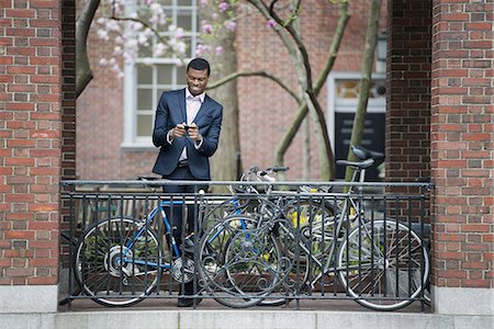 simsearch:6118-07122467,k - City life in spring. Young people outdoors in a city park. A man in a suit, beside a bicycle park on a sidewalk. Using his smart phone. Stockbilder - Premium RF Lizenzfrei, Bildnummer: 6118-07354567