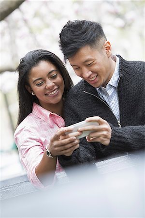 radio - City life in spring. Young people outdoors in a city park. A couple side by side, looking down at a smart phone. Stock Photo - Premium Royalty-Free, Code: 6118-07354570