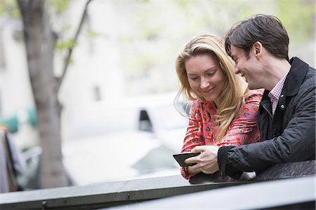 smart phone woman - City life in spring. Young people outdoors in a city park. Two people sitting side by side, looking down at a smart phone. Stock Photo - Premium Royalty-Free, Code: 6118-07354581