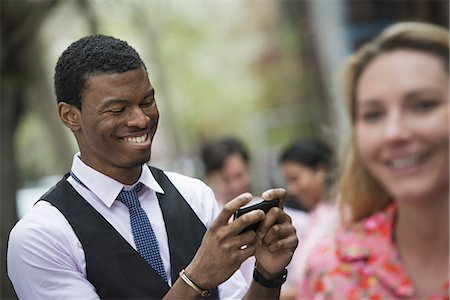 pink shirt woman - City life in spring. Young people outdoors in a city park. A man smiling as he looks at his phone, and a close of up of a woman with blonde hair. Stock Photo - Premium Royalty-Free, Code: 6118-07354584