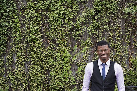 panachiert - City life in spring. City park with a wall covered in climbing plants and ivy.  A young man in a waistcoat, shirt and tie. Looking at the camera. Stockbilder - Premium RF Lizenzfrei, Bildnummer: 6118-07354588