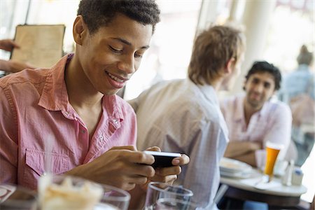 Urban Lifestyle. Three young men in a cafe. One checking his smart phone. Two talking at a table. Photographie de stock - Premium Libres de Droits, Code: 6118-07354531