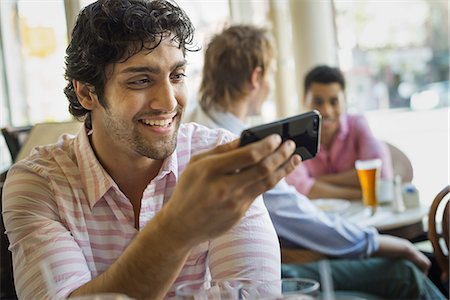 Urban Lifestyle. Three young men around a table in a cafe. One using his smart phone Stock Photo - Premium Royalty-Free, Code: 6118-07354534