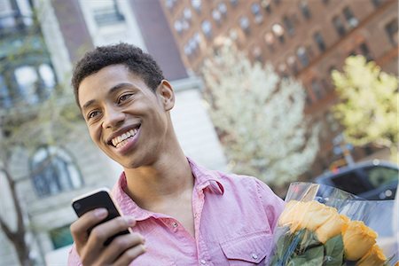 Urban Lifestyle. A young man with short black hair, wearing a pink casual shirt. Holding a smart phone. Stock Photo - Premium Royalty-Free, Code: 6118-07354538