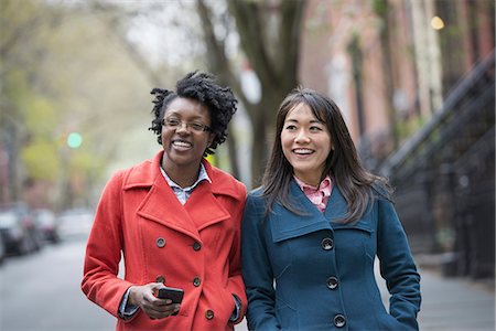 Two women side by side on a city street. One holding a cell phone. Stock Photo - Premium Royalty-Free, Code: 6118-07354657
