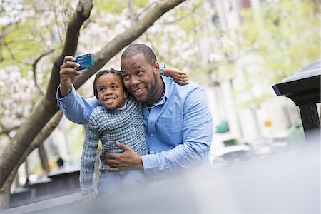 A New York city park in the spring. Sunshine and cherry blossom. A father and son side by side. Using a smart phone to take a picture. Fotografie stock - Premium Royalty-Free, Codice: 6118-07354690