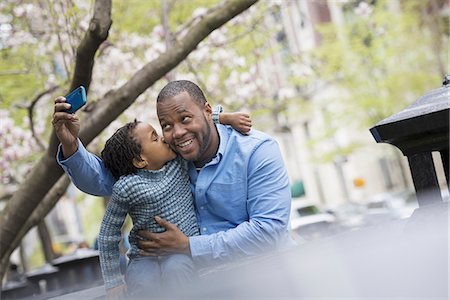 excited african american families - A New York city park in the spring. Sunshine and cherry blossom. A father and son side by side. Using a smart phone to take a picture. Stock Photo - Premium Royalty-Free, Code: 6118-07354691