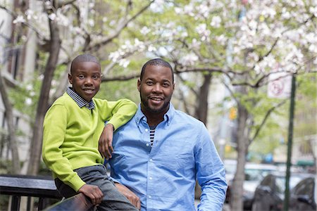 A New York city park in the spring. Sunshine and cherry blossom. A boy sitting on a fence, beside his father. Stock Photo - Premium Royalty-Free, Code: 6118-07354694
