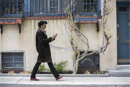 simsearch:6118-08842149,k - A woman in a warm coat walking along the street, checking her phone. Foto de stock - Royalty Free Premium, Número: 6118-07354628