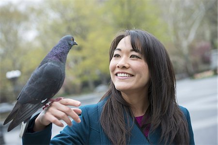 A young woman in the park with a pigeon perched on her wrist. Stock Photo - Premium Royalty-Free, Code: 6118-07354631