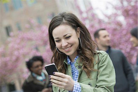 simsearch:6118-07203686,k - A young woman checking her smart phone for messages in the park. A group of friends in the background. Stock Photo - Premium Royalty-Free, Code: 6118-07354632