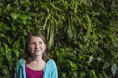 Outdoors in the city in spring. An urban lifestyle. A young girl standing in front of a wall covered with ferns and climbing plants. Stock Photo - Premium Royalty-Free, Code: 6118-07354754