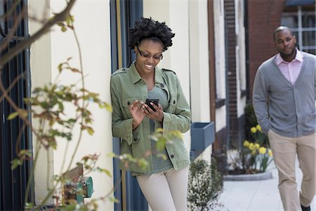 simsearch:6109-06007124,k - Outdoors in the city in spring. An urban lifestyle. A man approaching a woman who is checking her phone. Stock Photo - Premium Royalty-Free, Code: 6118-07354720
