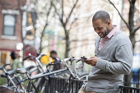 simsearch:6109-06007124,k - Outdoors in the city in spring. An urban lifestyle. A man using his phone. A group of people in the background. Cycle rack. Stock Photo - Premium Royalty-Free, Code: 6118-07354729