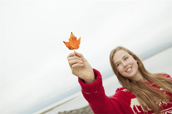 A day out at Ashokan lake. A young girl in a red winter knitted jumper holding up a maple leaf. Stock Photo - Premium Royalty-Free, Image code: 6118-07440271