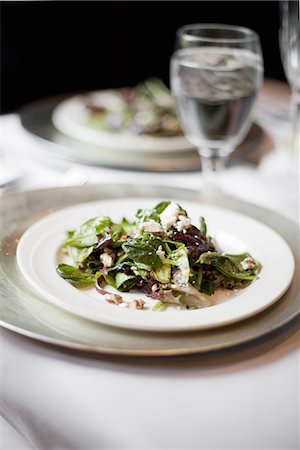 simsearch:6118-07440680,k - A formal table setting for a meal. China plates and glasses. An organic salad with mixed leaves. Foto de stock - Royalty Free Premium, Número: 6118-07440678