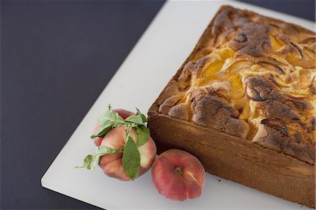 A square baked peach cake on a board with fresh peaches. Fruits. Organic fresh food on a farm stand with a herb garnish. Stock Photo - Premium Royalty-Free, Code: 6118-07440686