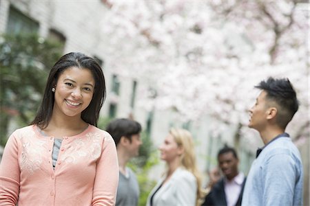 City life in spring. Young people outdoors in a city park. A woman in a pink shirt with four people in the background. Stock Photo - Premium Royalty-Free, Code: 6118-07440887