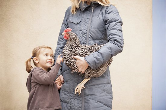 A woman in a grey coat holding a black and white chicken with a red coxcomb under one arm. A young girl beside her holding her other hand Stock Photo - Premium Royalty-Free, Image code: 6118-07440888