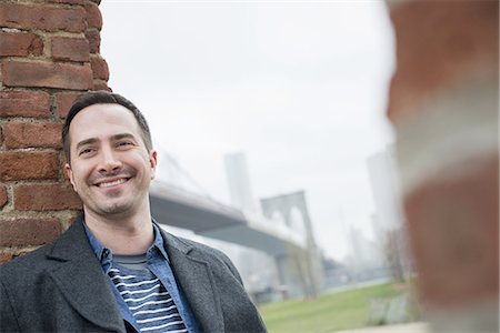 New York city. The Brooklyn Bridge crossing over the East River. A man leaning against a brick wall. Stock Photo - Premium Royalty-Free, Code: 6118-07440940