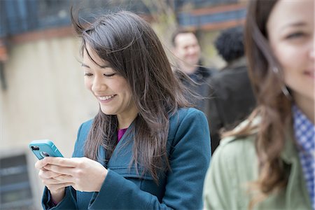 simsearch:6118-09165914,k - A woman checking her turquoise smart phone, among other people on a city street. Foto de stock - Royalty Free Premium, Número: 6118-07440937