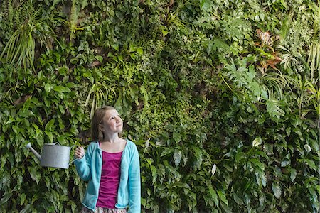 elementary age - A young girl standing in front of a wall covered with ferns and climbing plants. Stock Photo - Premium Royalty-Free, Code: 6118-07441051