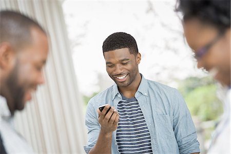 spring season and african american people - A young man checking his phone, behind a couple in the foreground. Photographie de stock - Premium Libres de Droits, Code: 6118-07441038