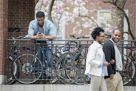 simsearch:6109-06007124,k - A bicycle rack with locked bicycles, a man texting and a couple walking by. Stock Photo - Premium Royalty-Free, Code: 6118-07441039