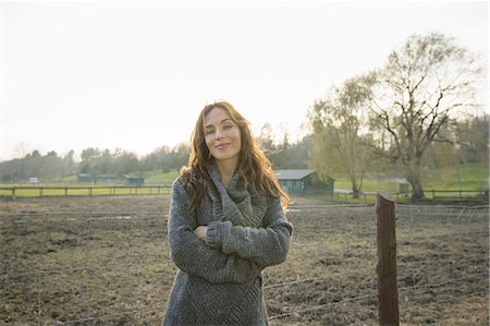 A woman standing with arms folded, by a paddock in an animal sanctuary. Stock Photo - Premium Royalty-Free, Code: 6118-07439826