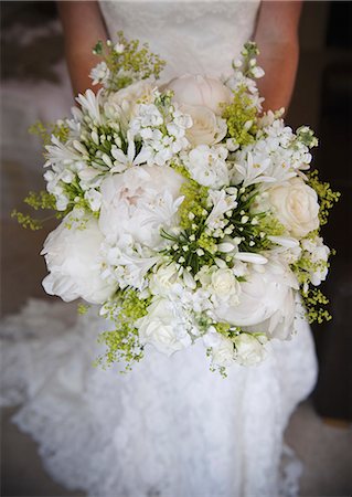 robe de mariée - A woman in a white dress, a bride holding a bridal bouquet of white flowers, large white roses and peonies, with delicate yellow flowers and green leaves. Photographie de stock - Premium Libres de Droits, Code: 6118-07521750