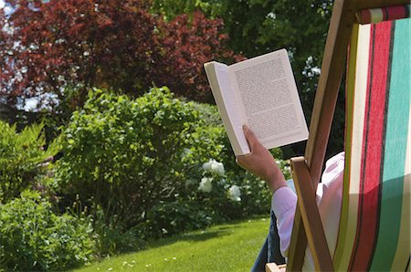 relaxing in backyard - A person sitting in a deckchair, reading. Stock Photo - Premium Royalty-Free, Code: 6118-07521770