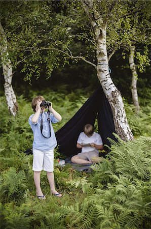 simsearch:6118-07808977,k - Two boys camping in New Forest. One sitting under a black canvas shelter.  One boy looking through binoculars. Foto de stock - Sin royalties Premium, Código: 6118-07521780