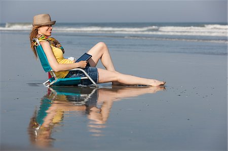 simsearch:6118-07203856,k - A woman in a sunhat and scarf on the beach on the New Jersey Shore, sitting holding a digital tablet. Foto de stock - Royalty Free Premium, Número: 6118-07521786