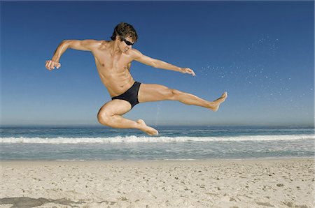 A young man doing a karate style leap on the beach in Cape Town. Stock Photo - Premium Royalty-Free, Code: 6118-07521804