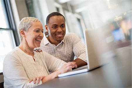 people office two man - Office life. Two people, a man and woman looking at a laptop screen and laughing. Stock Photo - Premium Royalty-Free, Code: 6118-07769498