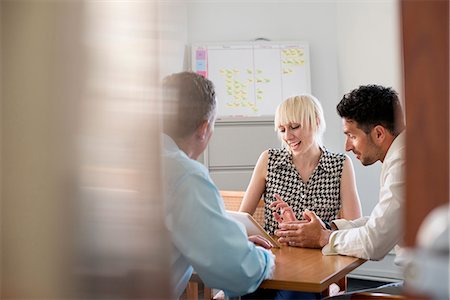 simsearch:6118-07769525,k - Three business colleagues in an office talking around a table and looking at a digital tablet. Foto de stock - Sin royalties Premium, Código: 6118-07769516