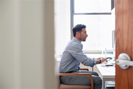 simsearch:6118-07769525,k - Office life. A man sitting at a desk using a computer, looking intently at the screen. Foto de stock - Sin royalties Premium, Código: 6118-07769523