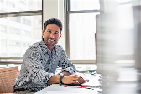 sinceridad - Office life. A man sitting at a desk using a computer, looking at the camera. Foto de stock - Sin royalties Premium, Código: 6118-07769527