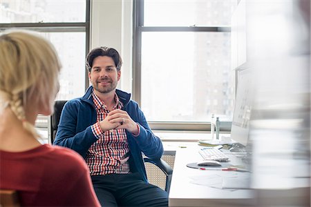 Office life. A man and woman in an office, seated talking to each other. Stock Photo - Premium Royalty-Free, Code: 6118-07769532