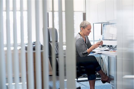 simsearch:614-08685284,k - A woman working in an office alone, checking her smart phone. Foto de stock - Sin royalties Premium, Código: 6118-07781643