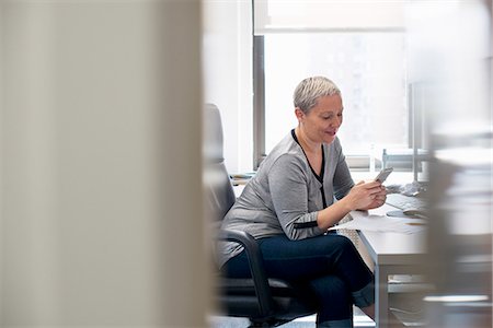 simsearch:6118-07781640,k - A woman working in an office alone, checking her smart phone. Fotografie stock - Premium Royalty-Free, Codice: 6118-07781642