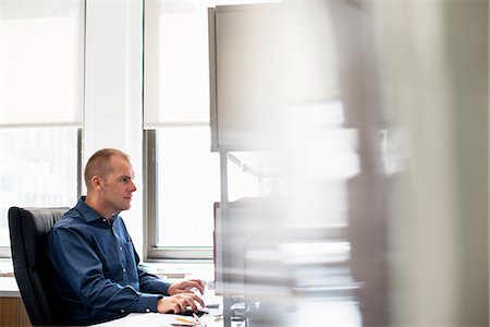 person sitting in chairs at desk side view - A man working in an office at a desk using a computer mouse. Focusing on a task. Stock Photo - Premium Royalty-Free, Code: 6118-07781646