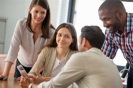 Four people, men and women, grouped around a digital tablet, looking at the screen. Stock Photo - Premium Royalty-Free, Code: 6118-07781679