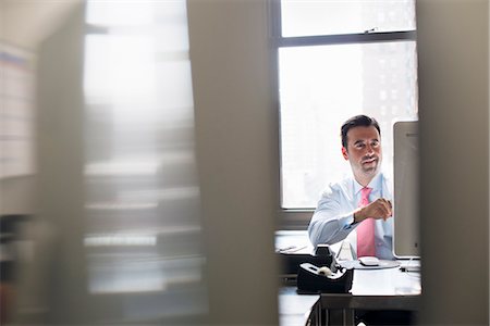 A man in shirt and tie seated at a desk looking at a computer screen. Stock Photo - Premium Royalty-Free, Code: 6118-07781633