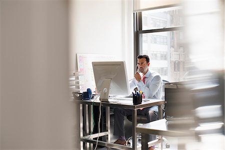 simsearch:6118-07781630,k - A man seated at a desk in an office, using a computer. Fotografie stock - Premium Royalty-Free, Codice: 6118-07781630