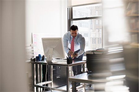 simsearch:6118-07781630,k - A man standing at his desk using his phone, dialling or texting. Fotografie stock - Premium Royalty-Free, Codice: 6118-07781631