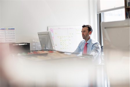 distance office - A man seated at an office desk using a computer. A wall chart with post it adhesive notes. Stock Photo - Premium Royalty-Free, Code: 6118-07781636