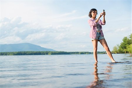 A woman standing in a lake in summer. Taking a photograph. Stock Photo - Premium Royalty-Free, Code: 6118-07781763