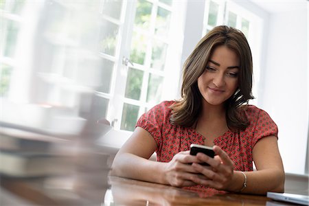 simsearch:6118-07781850,k - A woman seated at a table, checking her smart phone. Photographie de stock - Premium Libres de Droits, Code: 6118-07781767