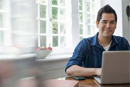 simsearch:6118-07781767,k - A man using a laptop seated at a table by a window. Working from home. Stock Photo - Premium Royalty-Free, Code: 6118-07781765